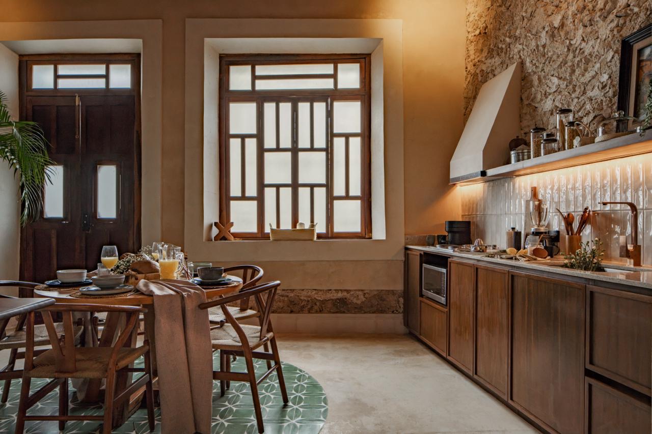 Cocina y comedor de Casa Lourdes con celosías de madera y muro de piedra